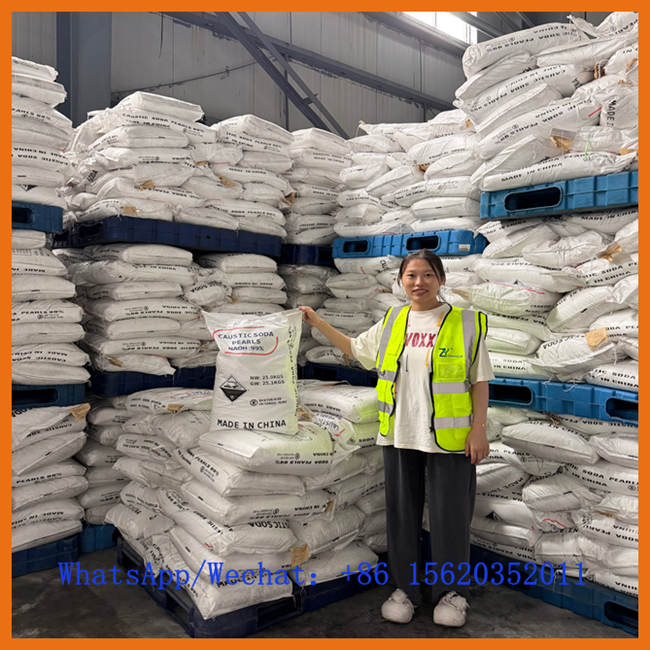 Une employée vêtue d'un gilet de sécurité réfléchissant se tient à côté d'une pile de sacs de perles de soude caustique. Elle pose avec un sac portant l'étiquette détaillée du produit. Des informations de contact Whatsapp/Wechat sont superposées.